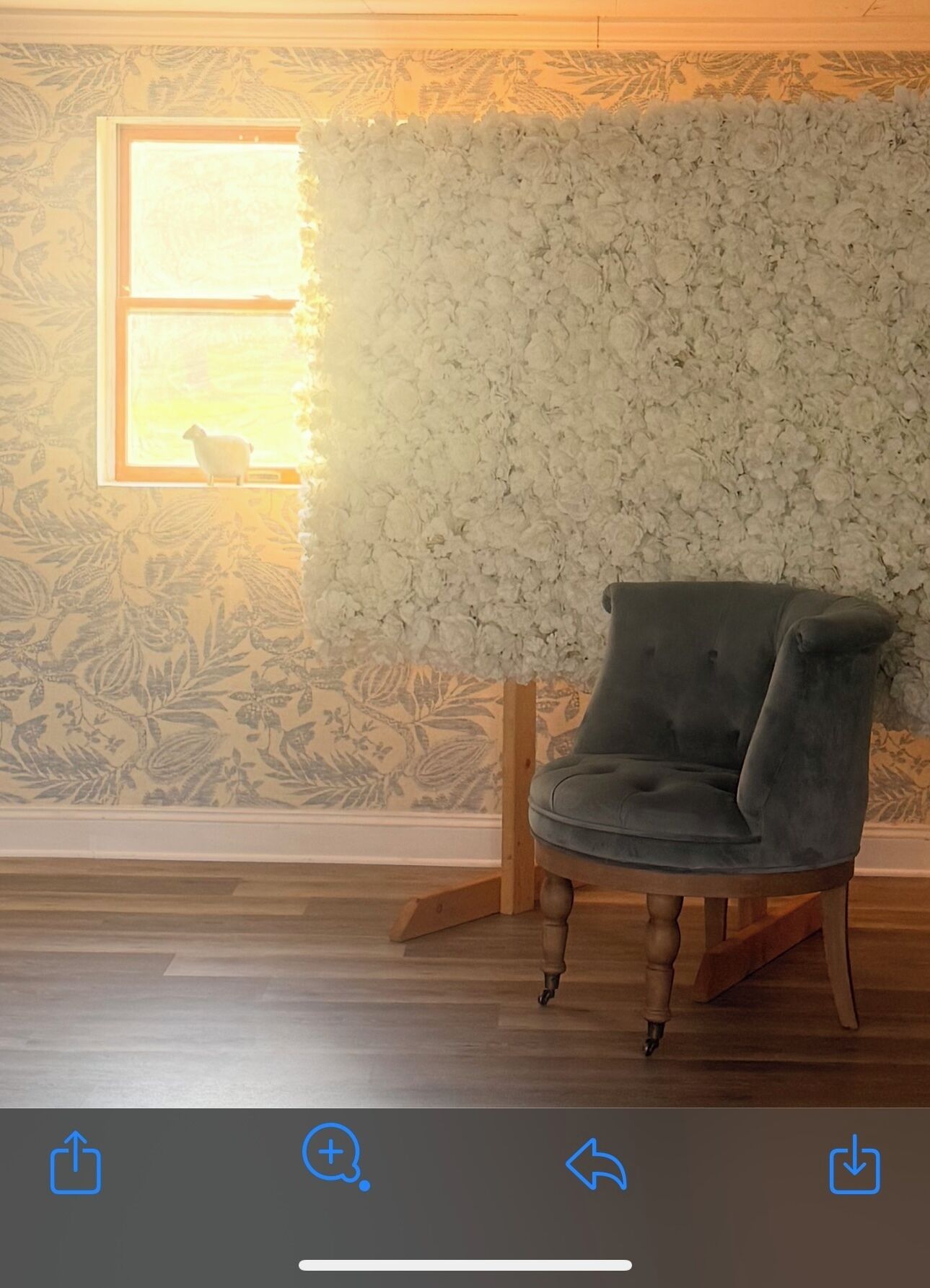 Une pièce avec un mur décoré de motifs floraux, une fenêtre donnant sur un beau paysage et un fauteuil gris.