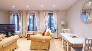 A living room with a sofa, a TV, a table, and a window with curtains. - Central Apartment with Parking by Guestz (Chester)