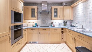 A kitchen with wooden cabinets, a stainless steel range hood, a double oven, a sink, and a tiled backsplash. - Central Apartment with Parking by Guestz (Chester)