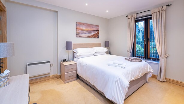 A bedroom with a bed, bedside tables, a radiator, a window with curtains, and a painting on the wall. - Central Apartment with Parking by Guestz (Chester)