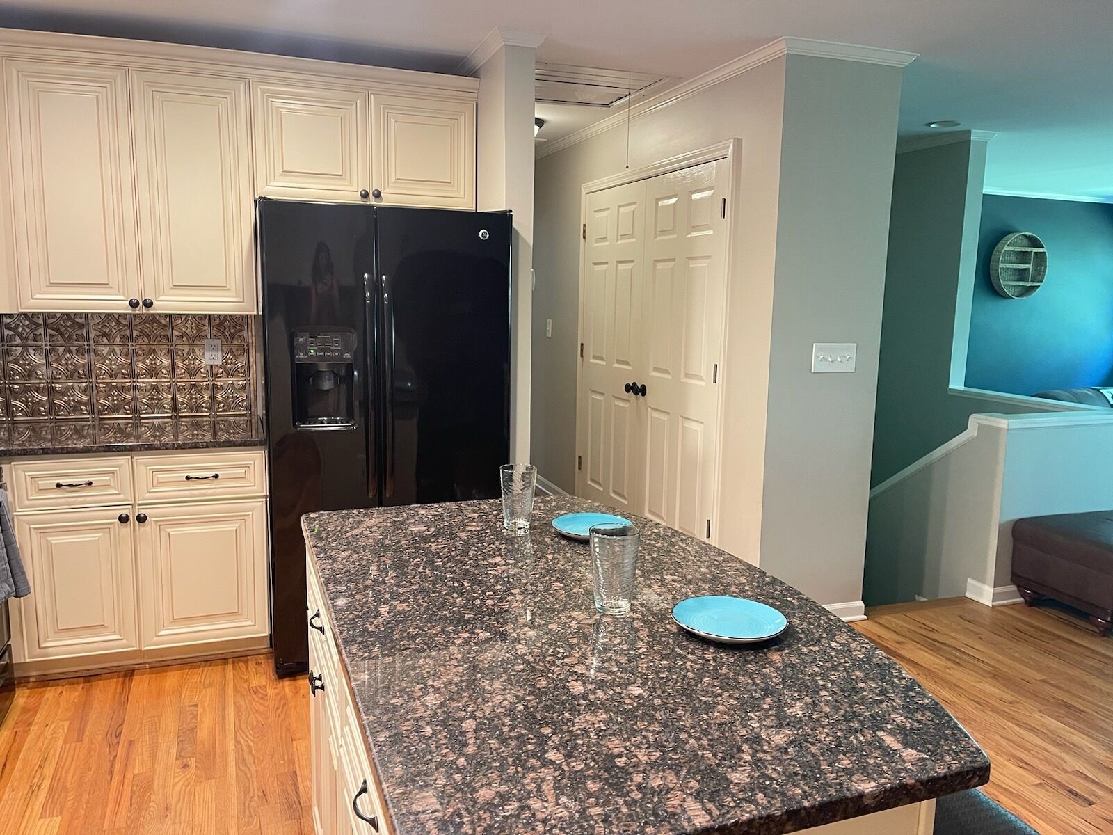 A kitchen with white cabinetry, a black refrigerator, granite countertops, and a blue wall.