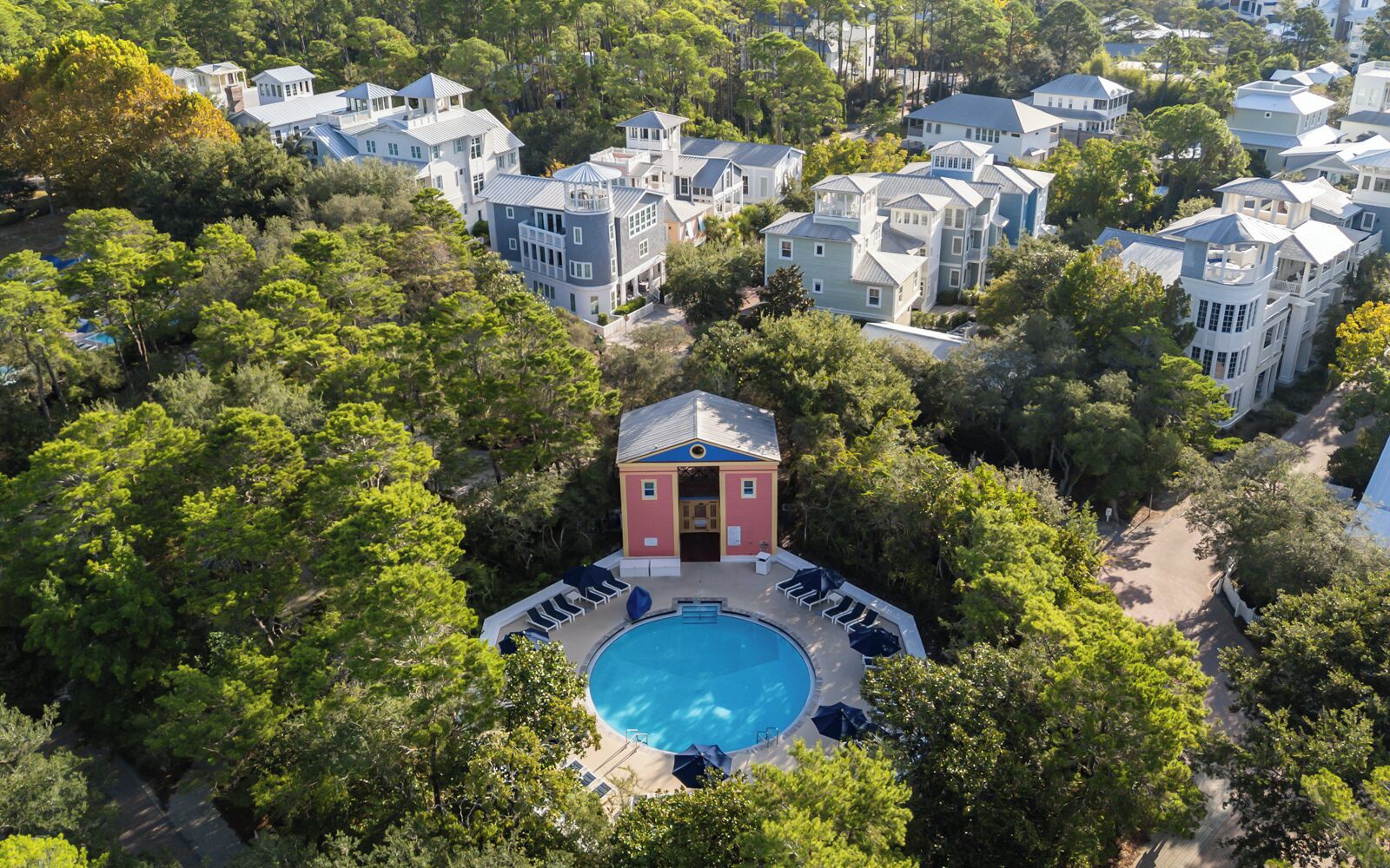 Vista aérea de una zona residencial con un edificio central que cuenta con una piscina rodeada de sillones de descanso.