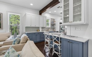 A modern kitchen with white cabinets, a bar area, and a dining space with a sofa. - The Poppy House + Seaside, Pet Friendly & Bikes (Santa Rosa Beach)