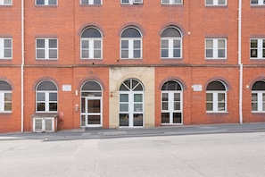 A red brick building with multiple windows, a central entrance with a door, and a fire hydrant on the sidewalk. - Thornhill House by Guestz (Wakelfield)