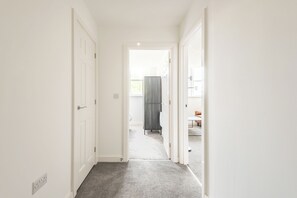 A narrow hallway with a carpeted floor, white walls, and a door leading to a room with a visible window. - Thornhill House by Guestz (Wakelfield)