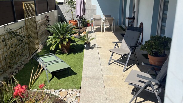 Un patio con césped verde, plantas en macetas y mobiliario exterior.