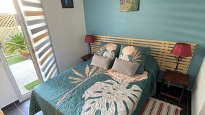 Un dormitorio con cama, mesita de noche, lámpara, un cuadro y vistas al exterior.
