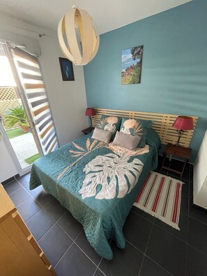 A bedroom with a bed, a nightstand, a lamp, a painting, and a view of the outside. - Quiet RDJ apartment, All amenities Porte Marine area (La Seyne-sur-Mer)