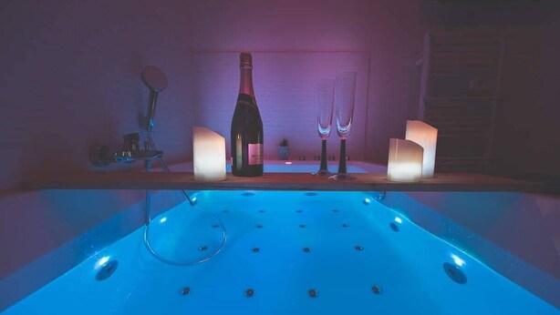 Eine Badewanne mit blauem Licht, einer Flasche und zwei Gläsern auf einem Regal.