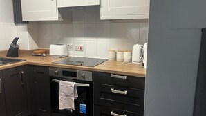 Uma cozinha com armários brancos, bancada com chaleira, torradeira e cafeteira. Há uma pia, suporte para facas e escorredor de louça.