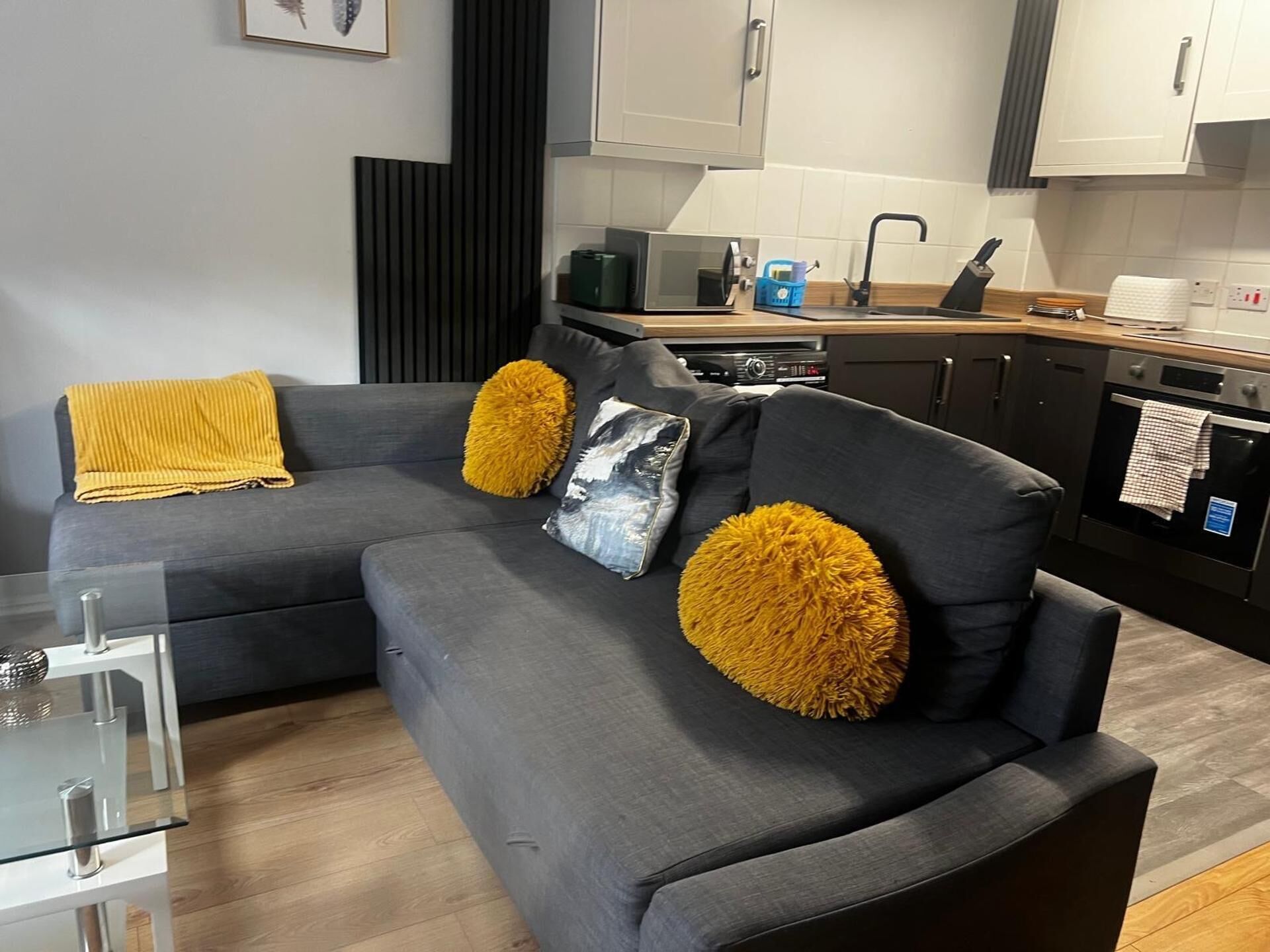 Una sala moderna con un sofá seccional gris, dos almohadones color mostaza y una mesa de centro de vidrio.