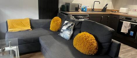 Una sala moderna con un sofá seccional gris, dos almohadones color mostaza y una mesa de centro de vidrio.