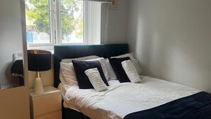 Un dormitorio con cama, lámpara de noche y ventana con vista a árboles.