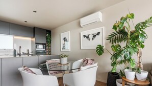 Een moderne keuken met een eethoek, met een ronde glazen tafel, witte stoelen en een grote potplant.