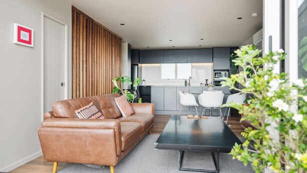 A modern living room with a leather sofa, a coffee table, and a view into the kitchen. - Stylish 1BD Flat & Car Park, Deck + Harbour Views (Auckland)