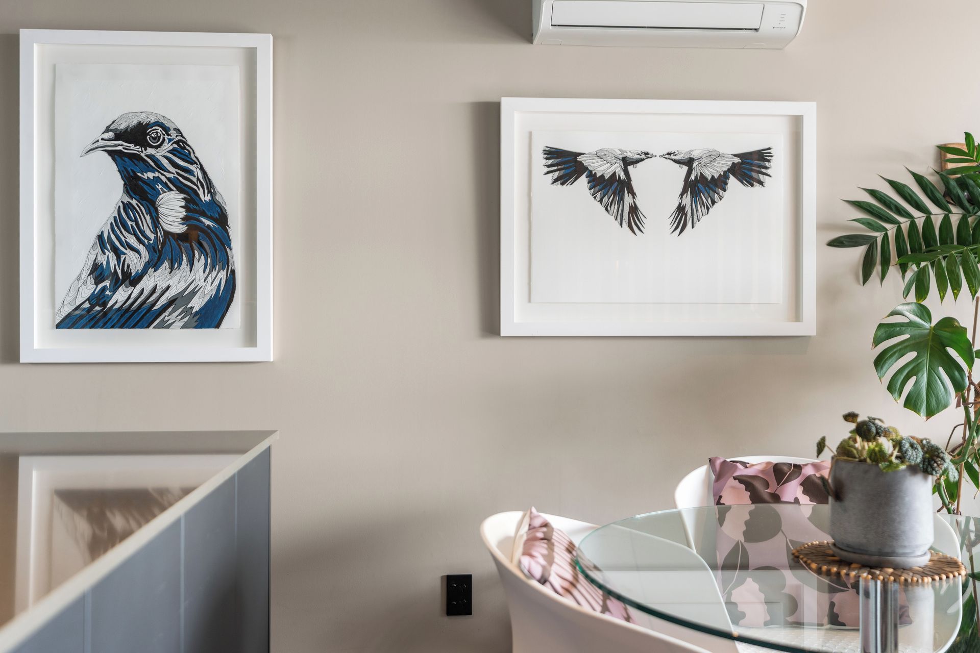 A room with a dining table, a potted plant, and two framed bird artworks on the wall.