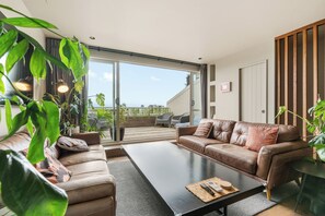 A modern living room with a brown leather sofa, a black coffee table, and a sliding glass door leading to a balcony. - Stylish 1BD Flat & Car Park, Deck + Harbour Views (Auckland)
