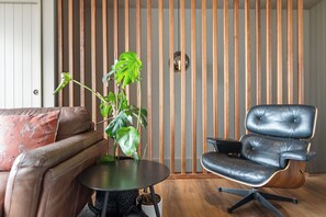 A modern living room with a brown leather sofa, a black leather armchair, a round black table, and a large green plant. - Stylish 1BD Flat & Car Park, Deck + Harbour Views (Auckland)