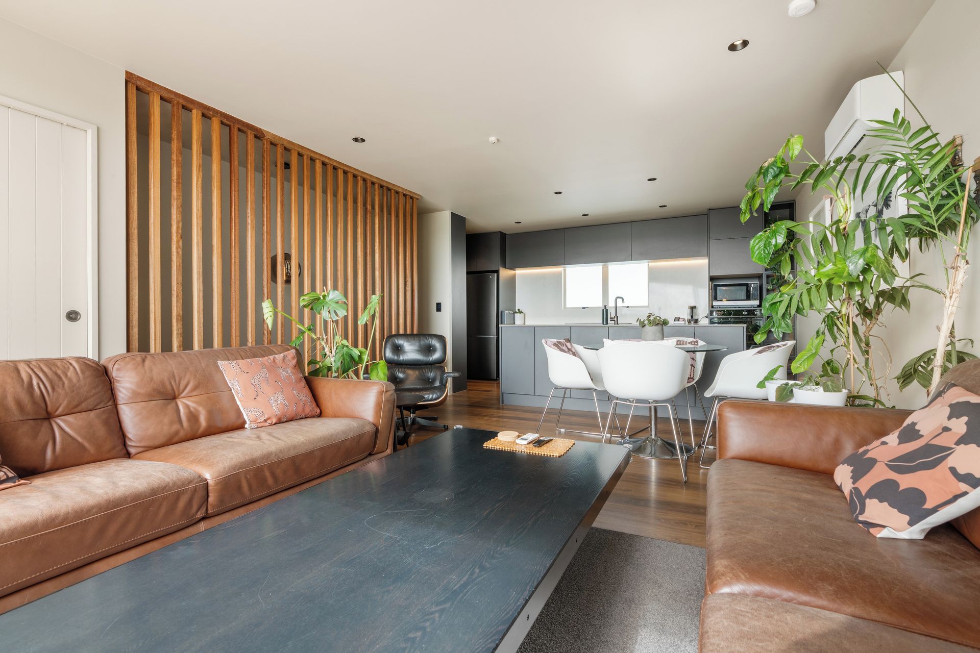 A modern living room with a brown leather sofa, a black coffee table, and a dining area with white chairs.