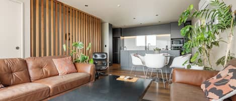 A modern living room with a brown leather sofa, a black coffee table, and a dining area with white chairs.