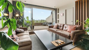 A modern living room with a brown leather sofa, a black coffee table, and a sliding glass door leading to a balcony. - Stylish 1BD Flat & Car Park, Deck + Harbour Views (Auckland)