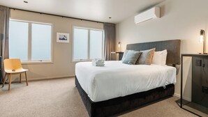 A hotel room with a large bed, a desk, a chair, and an air conditioning unit. - Stylish 1BD Flat & Car Park, Deck + Harbour Views (Auckland)