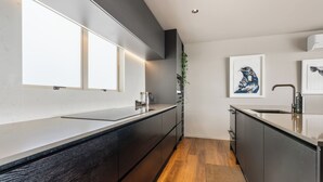 Een moderne keuken met donkere kastjes, een lang aanrecht en een houten vloer.