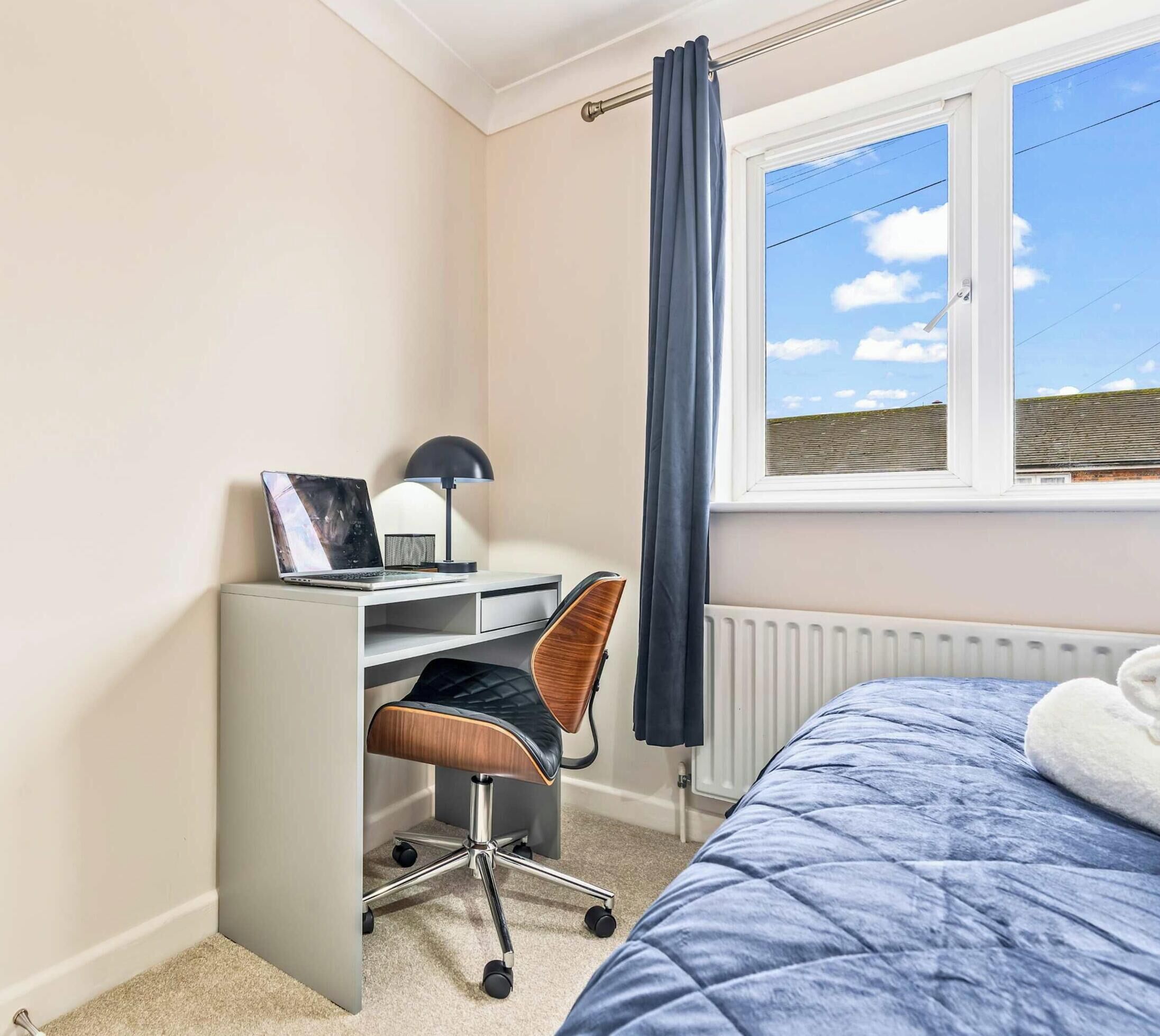 Ein Schlafzimmer mit Bett, Schreibtisch, Stuhl, Heizkörper und einem Fenster mit Vorhängen.