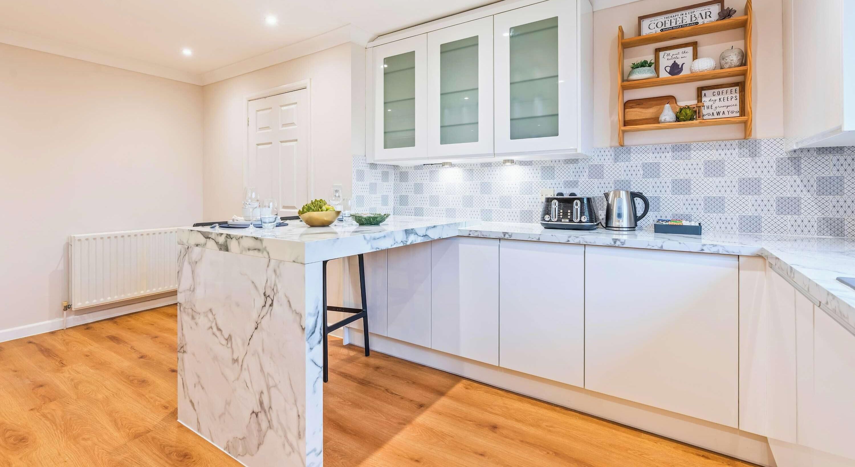 A modern kitchen with white cabinets, a marble countertop, and a coffee bar.