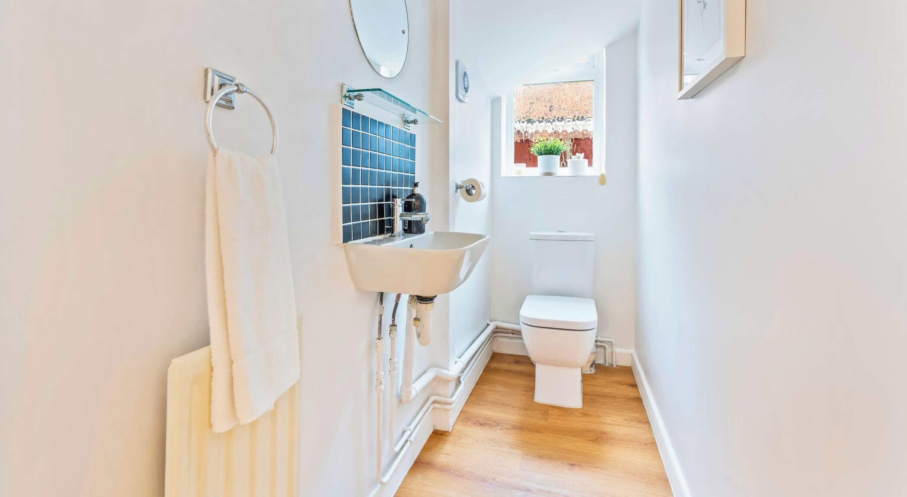 Un baño estrecho con un lavabo, inodoro y perchero blancos.