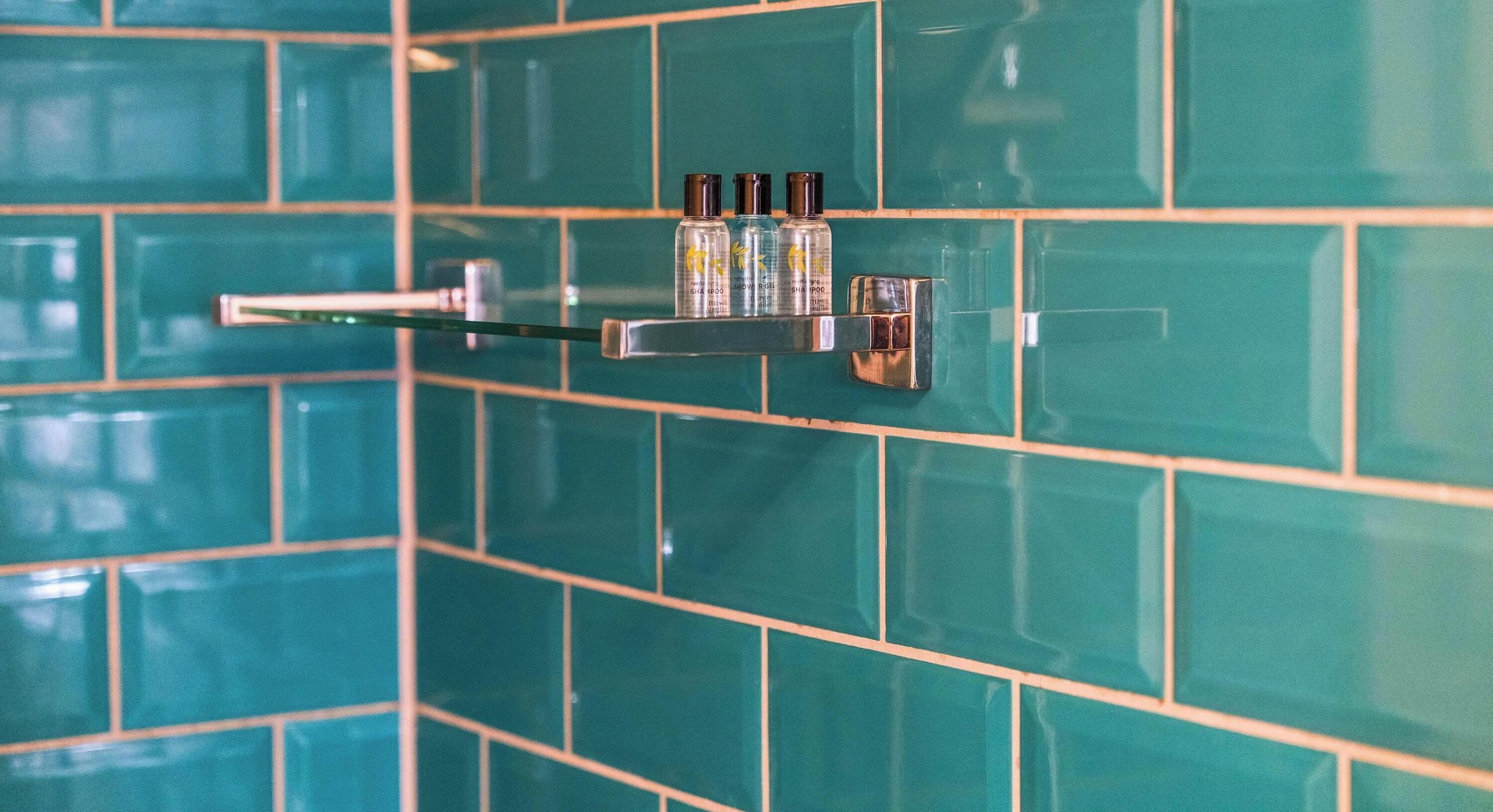 A bathroom with teal tiles, a chrome towel rack, and three bottles of shampoo.