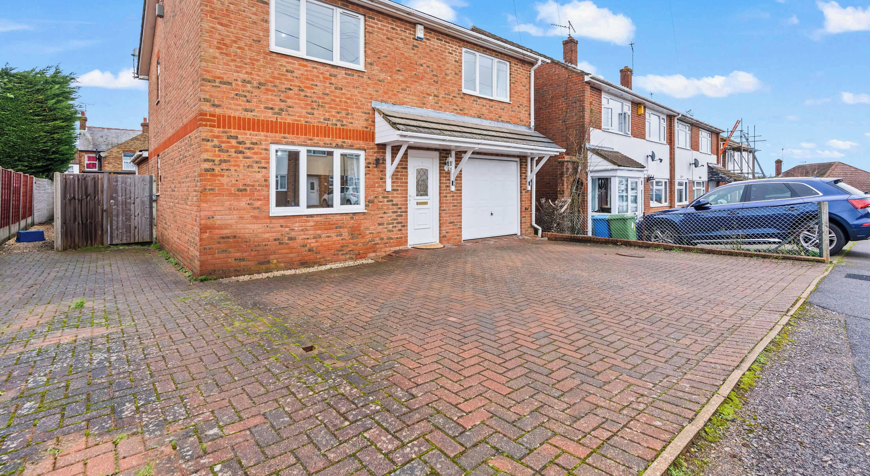 A residential brick house with a garage, a paved driveway, and a fenced area.