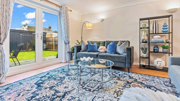A modern living room with a glass coffee table, a grey sofa with decorative pillows, a patterned rug, and a bookshelf with decorative items. - Cozy Family & Contractor Home, 3X FREE Parking by Redwood Stays (Hampshire)