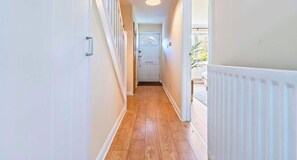 A narrow hallway with wooden flooring, white walls, and a white door at the end.