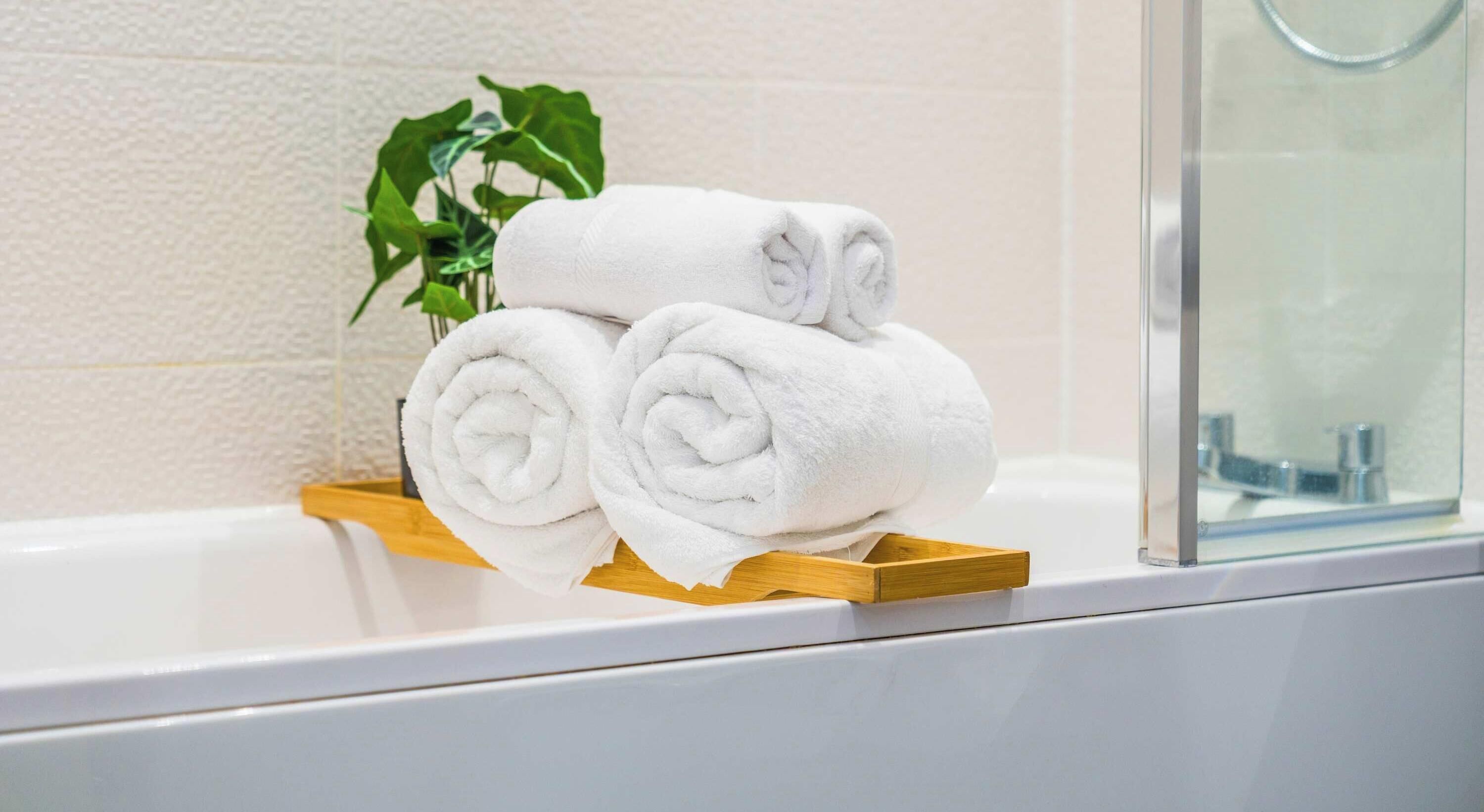 A bathroom with a white bathtub, a wooden towel rack, and a green plant.