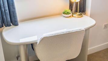 A white bathroom vanity with a towel hanging on the side, a small potted plant, and a floor lamp.
