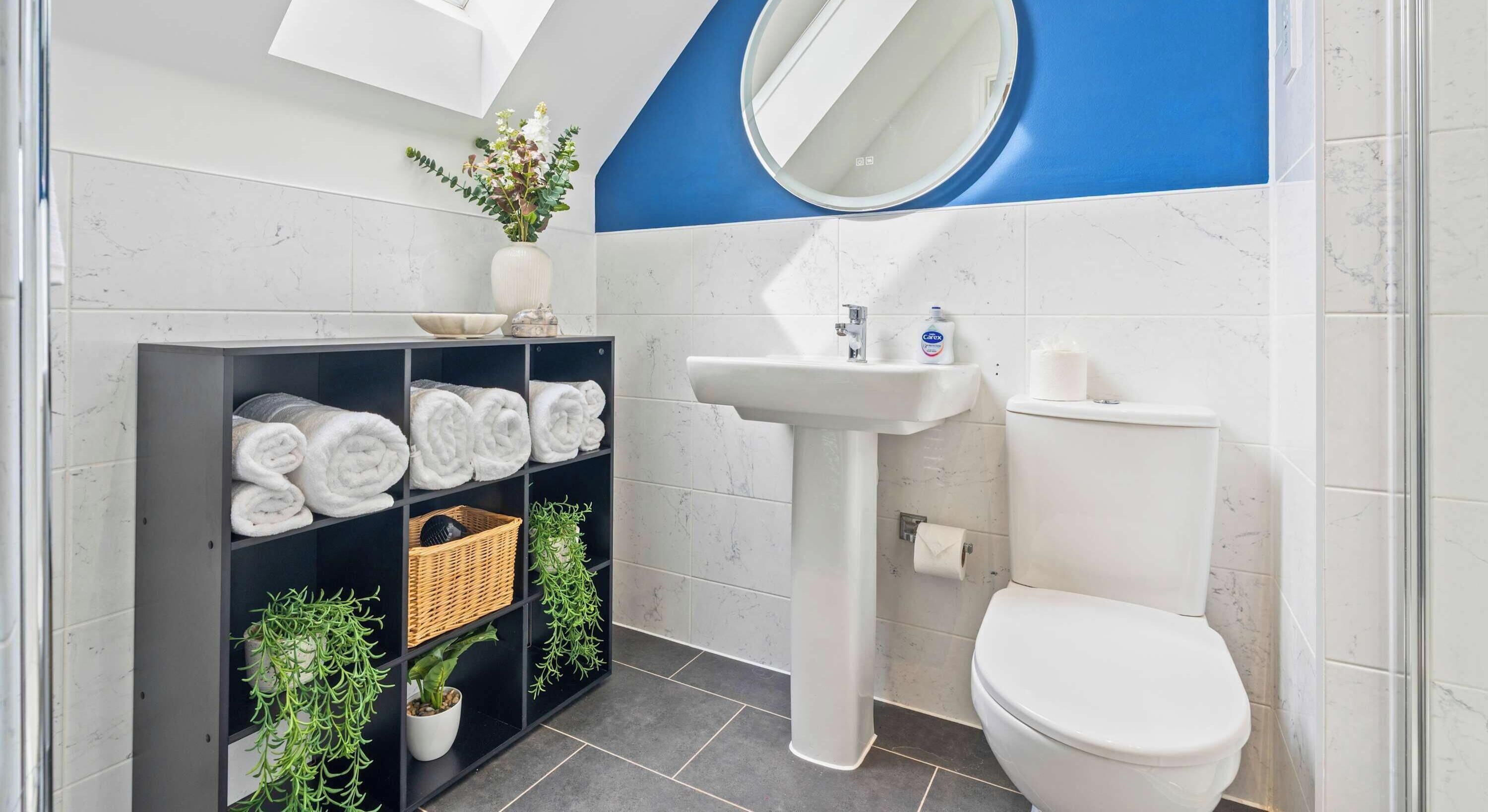 A bathroom with a white sink, toilet, and shelves with towels and plants.