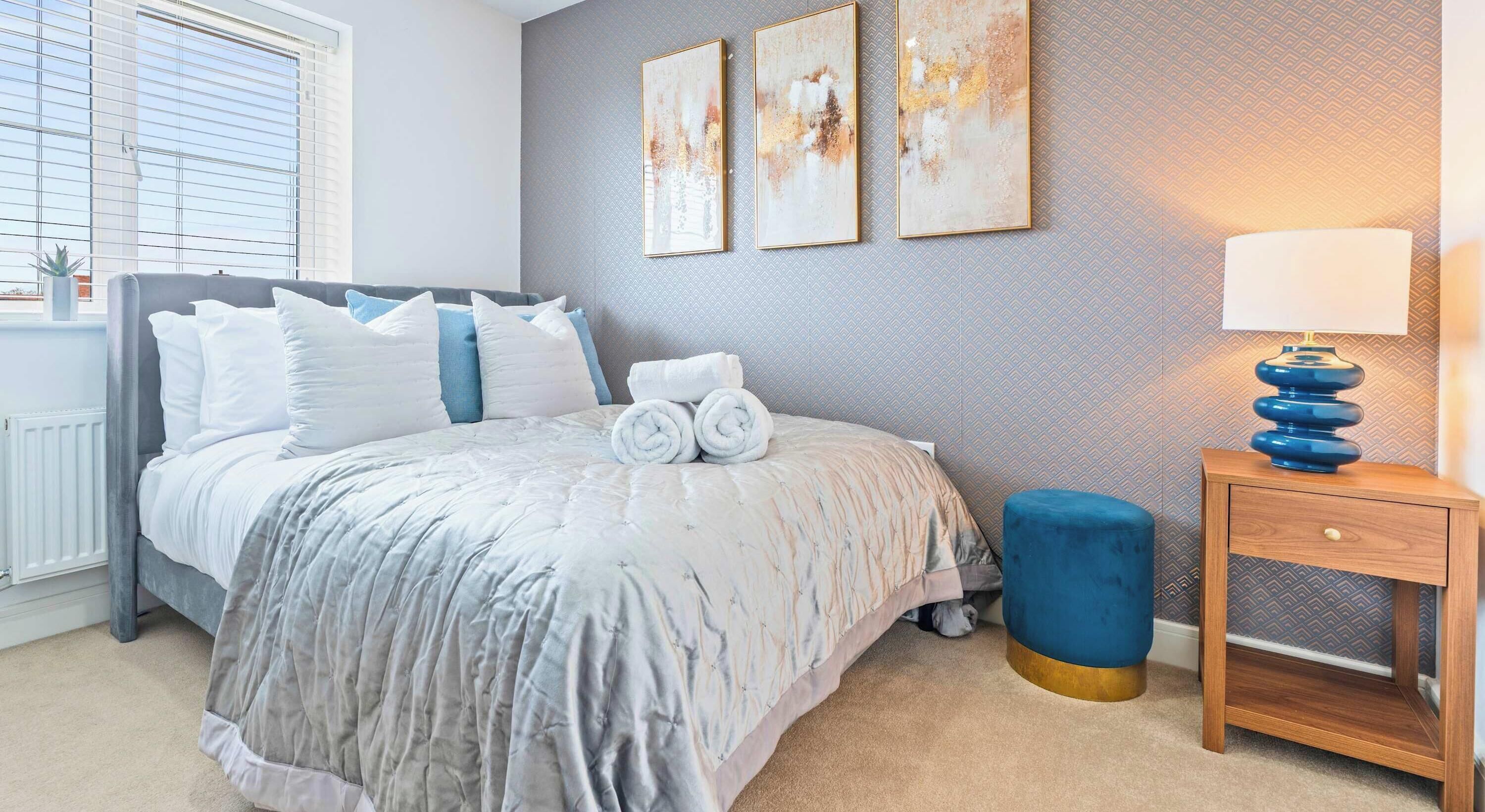 Une chambre à coucher avec un lit, des oreillers, une table de chevet avec une lampe et des œuvres d’art murales.
