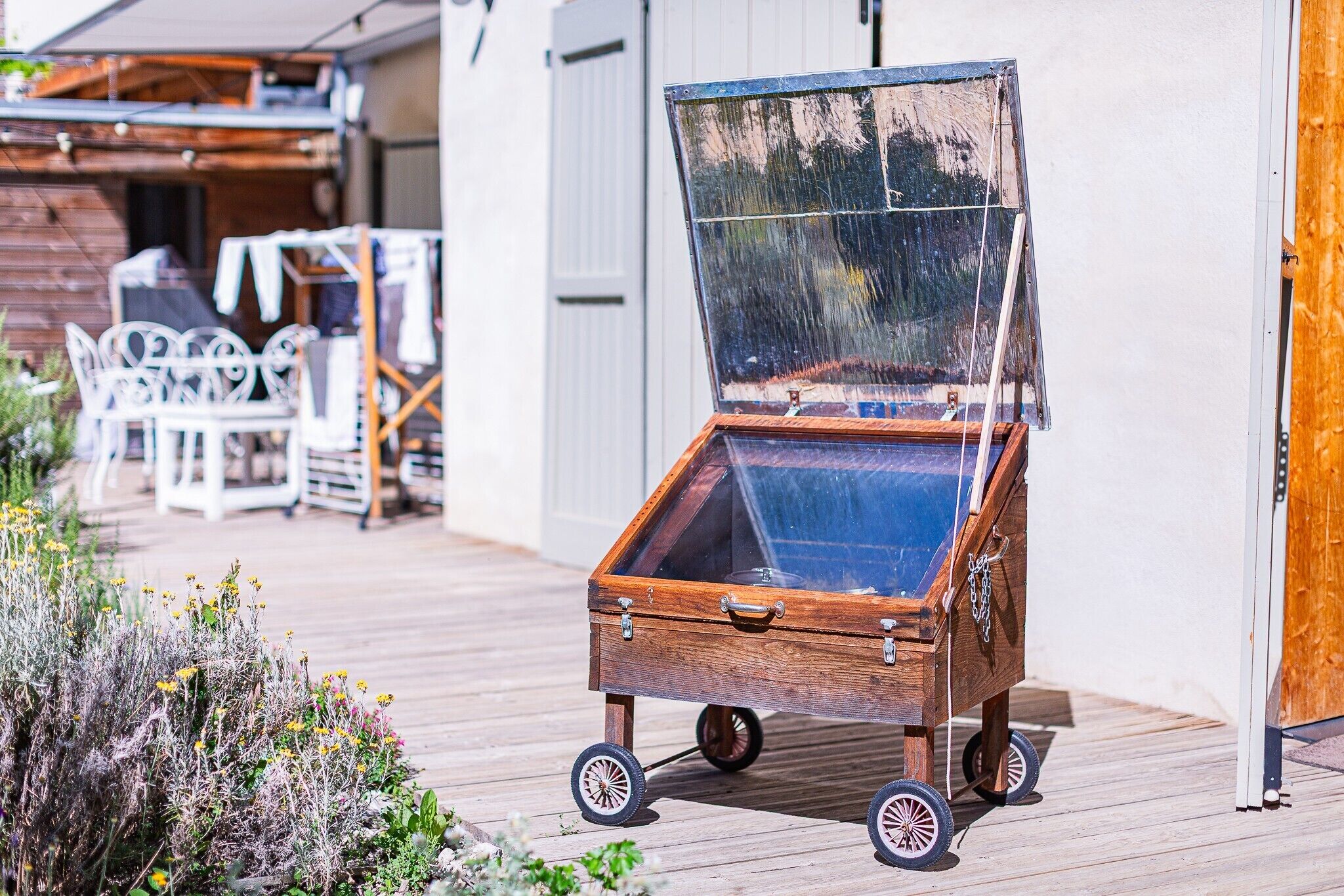 A wooden chest with wheels, a glass top, and a metal handle, placed on a wooden deck.