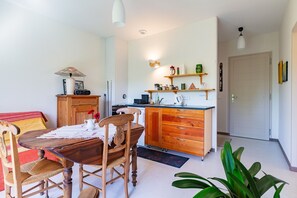 Un coin repas avec une table et des chaises en bois, une cuisine avec des placards en bois et une porte donnant sur une autre pièce.