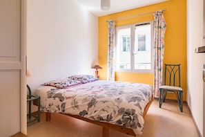 A bedroom with a bed, a chair, a window with curtains, and a lamp.