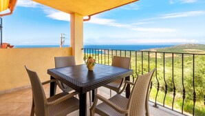 Un balcon avec une table et des chaises, un vase rempli de fleurs et une vue sur la mer et les collines.