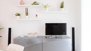 A modern living room with a flat-screen TV, a grey entertainment unit, and white shelves with plants. - Pigneto Rooftop: Elegant Two-Level Penthouse with Spacious Terraces (Roma)