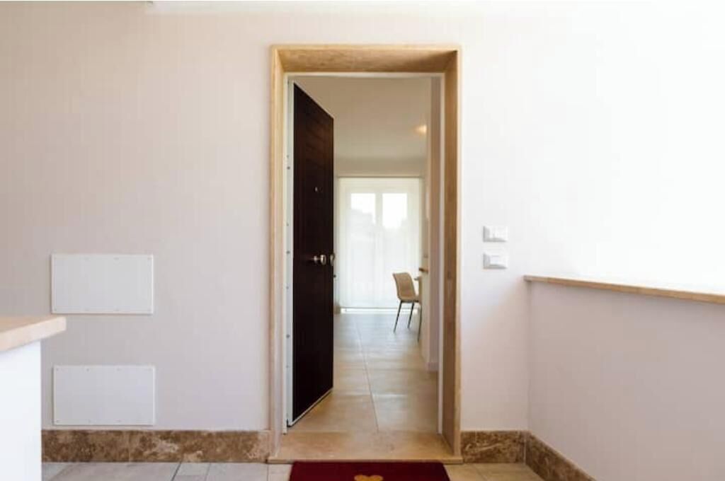 A hallway with a door leading to a room, a chair, and a light switch on the wall.