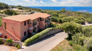 A two-story building with a red-tiled roof, a balcony on the second floor, and a view of the sea. - Sea View Isola Rossa Apartment with Sea View, Wi-Fi, and Air Conditioning (Paduledda)