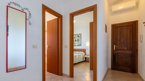 A hallway with wooden doors leading to a bedroom with a bed and a nightstand. - Sea View Isola Rossa Apartment with Sea View, Wi-Fi, and Air Conditioning (Paduledda)
