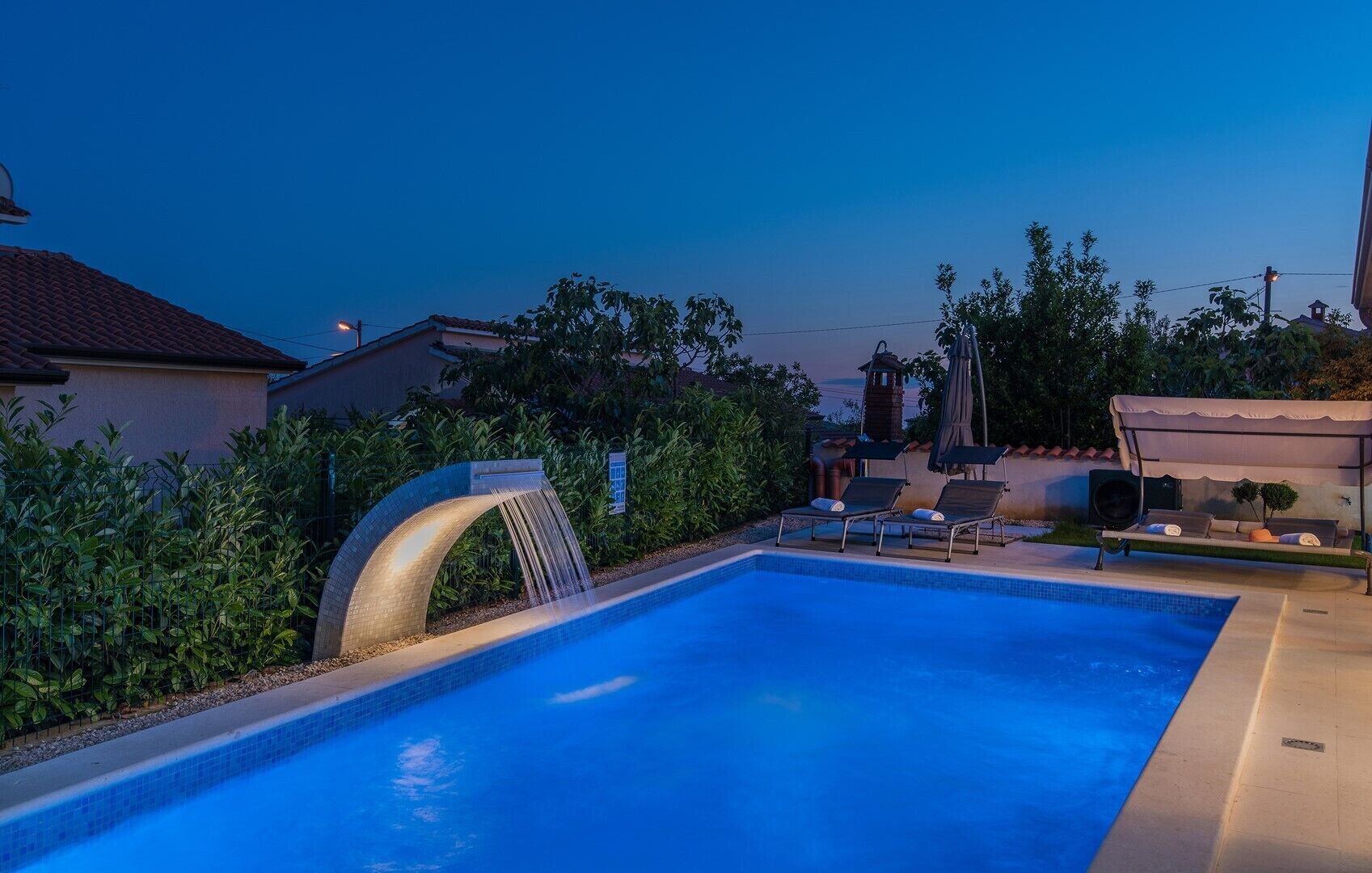 Ein Swimmingpool mit Wasserfall, Liegestühlen und einer überdachten Sitzgelegenheit.