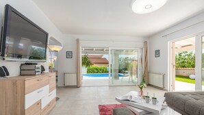 Una sala moderna con un televisor de pantalla plana, una mesa de centro, un sofá y vistas a una piscina y zona exterior.