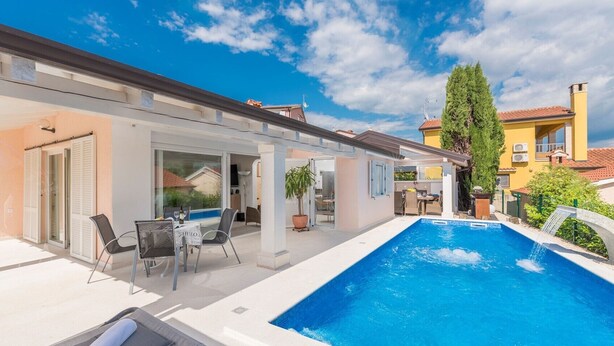 Una piscina con zona de patio, espacio de estar techado y vistas a edificios vecinos.