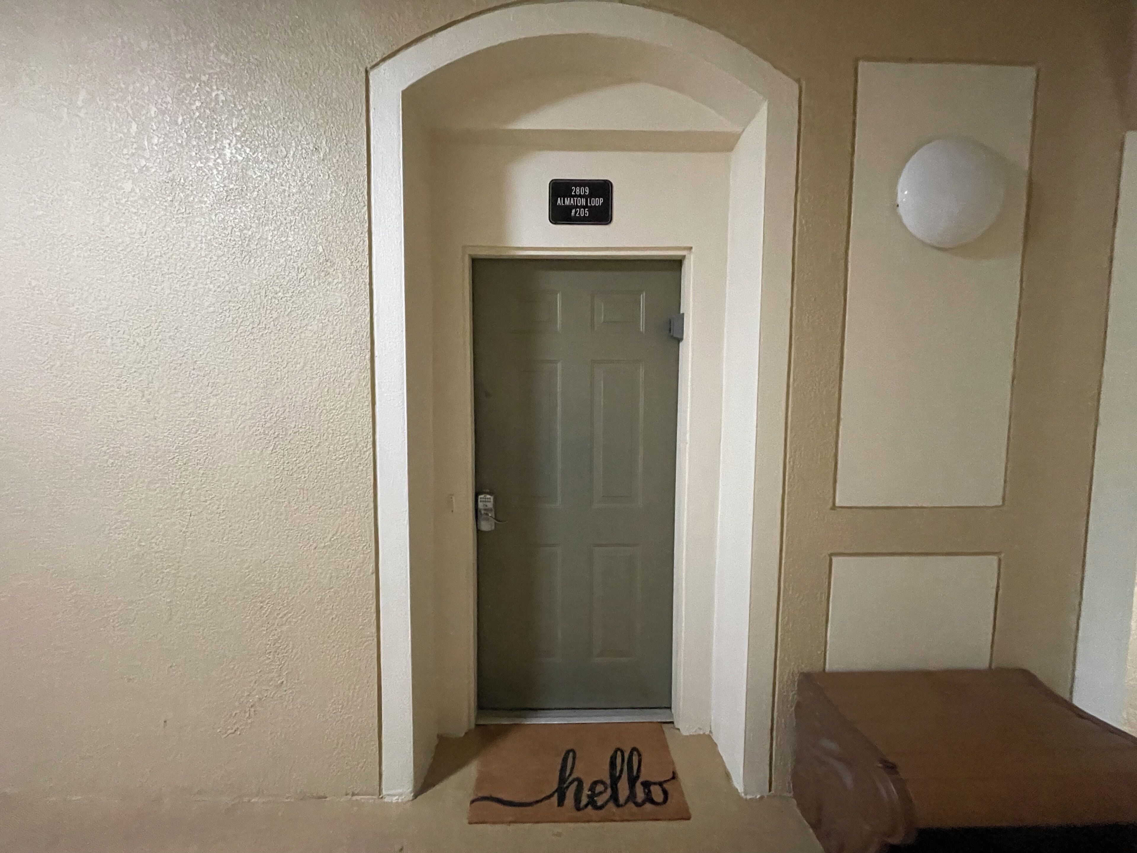 Un pasillo con una puerta etiquetada 'ALMATON LOOP #205' y un felpudo que dice 'hola' en la entrada.